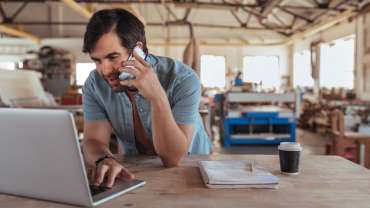 A sole trader in a phone call inside his workshop.