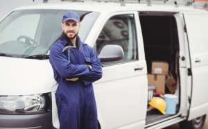 A carpenter holding a hammer standing outside his van.