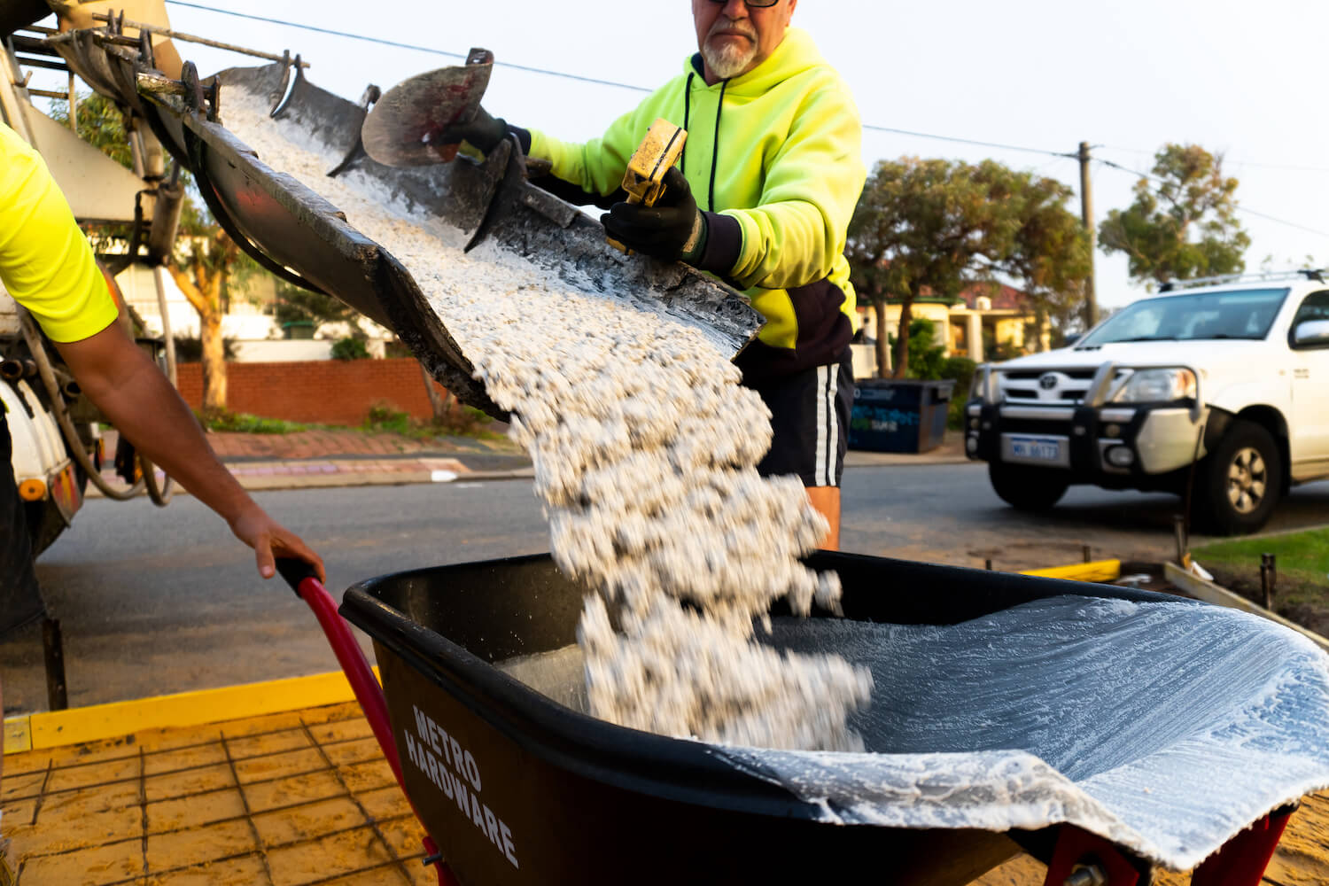 Workers fulling up a wheelbarrow full of concrete.