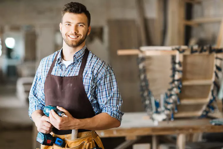 Carpenter holding a drill in his workshop smiling