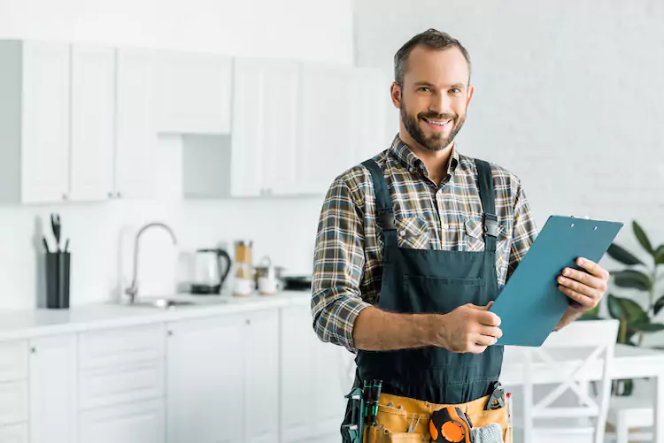 Plumber holding clipboard in a kitchen smiling