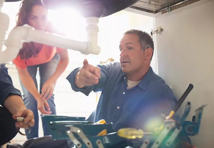 Plumber pointing at a pipe under the sink