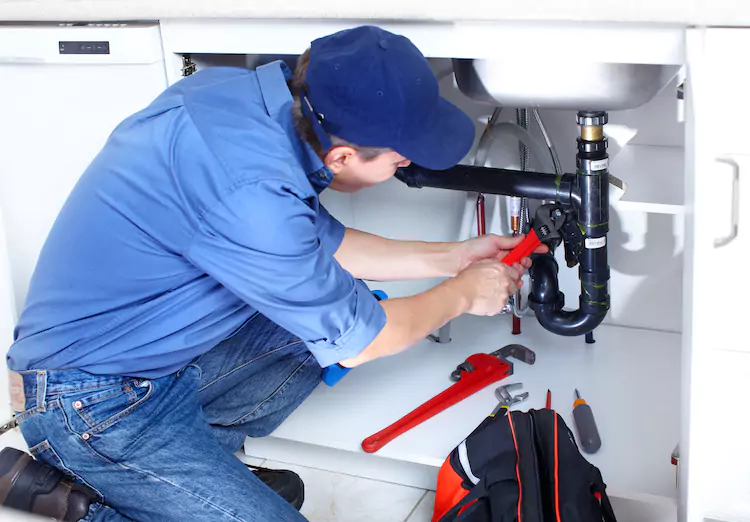 Plumber using a wrench to adjust a bolt under a sink