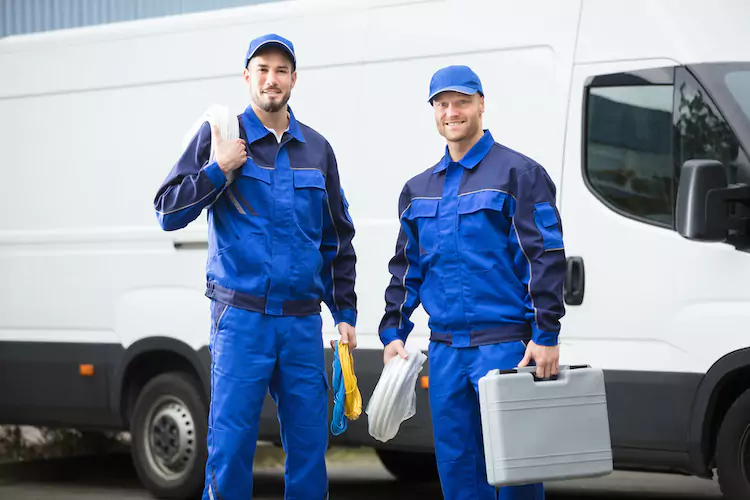 Insured electricians standing in front of their commercial vehicle holding tools and equipment