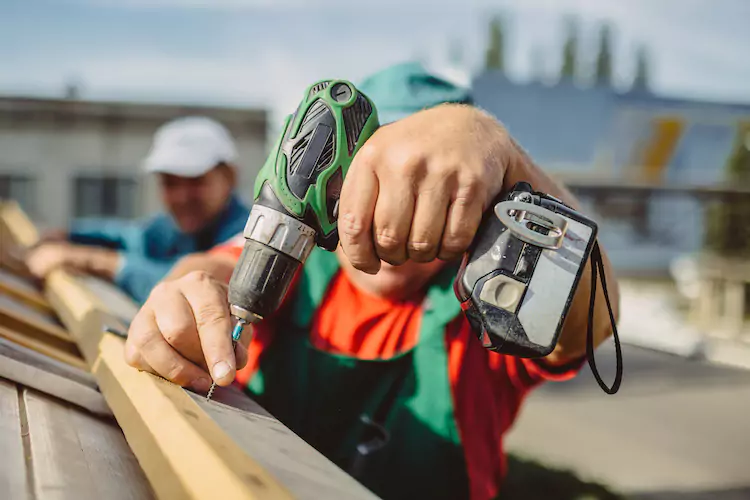 Insured roofer using a drill to drill in a wooden beam