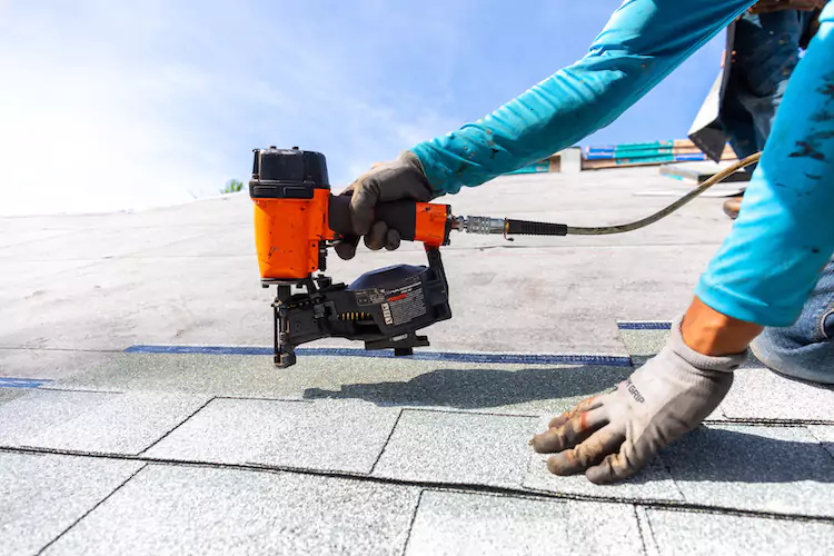 Roofer using a nail gun to nail in a roof tile
