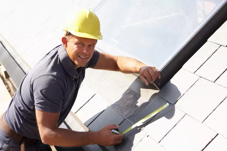 Insured roofer standing on a roof using a tape measure to measure tiles