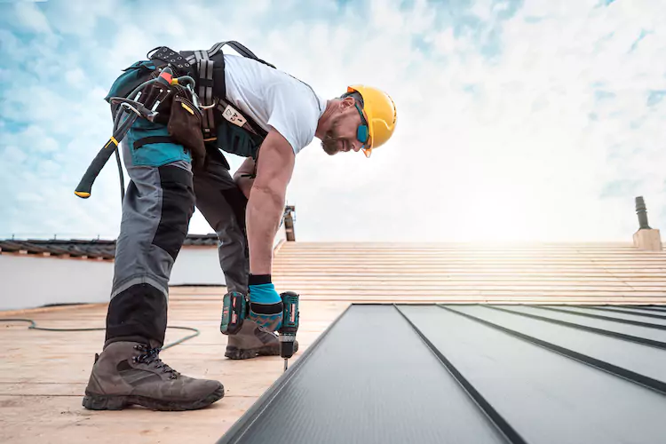 Insured roofer on a roof drilling into tiles wearing a yellow hardhat