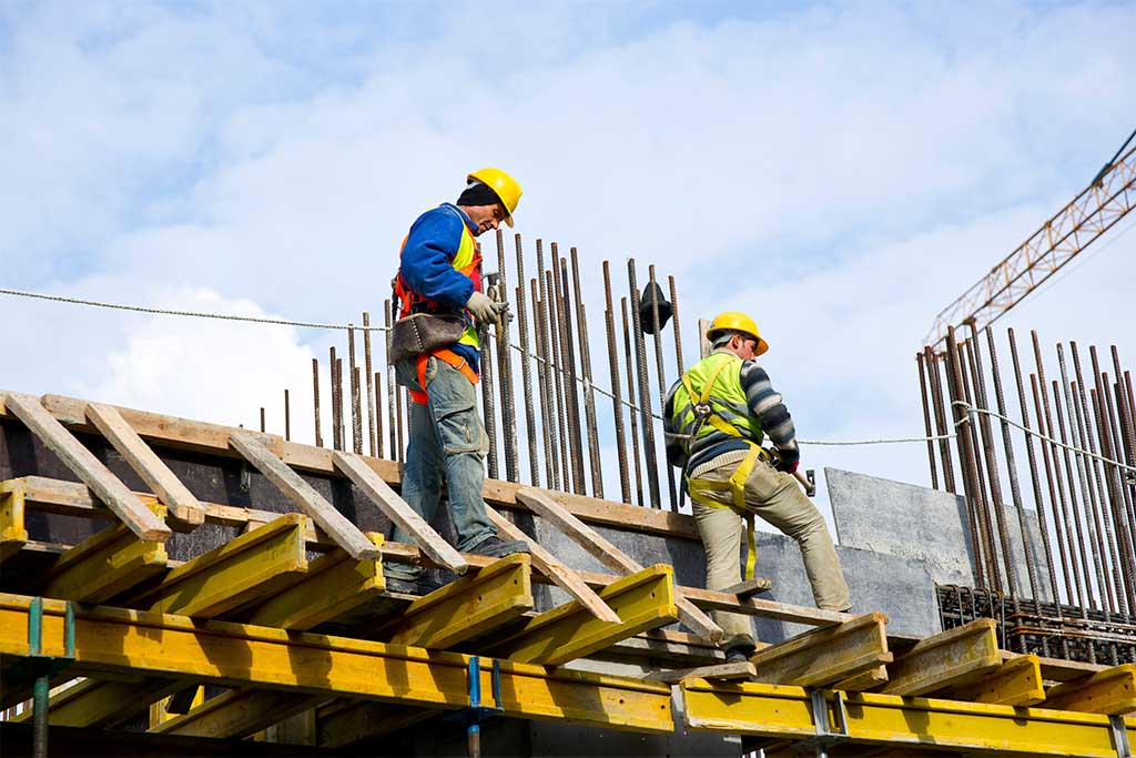 Top view of two smiling engineers in safety helmets, posing together on a construction site.