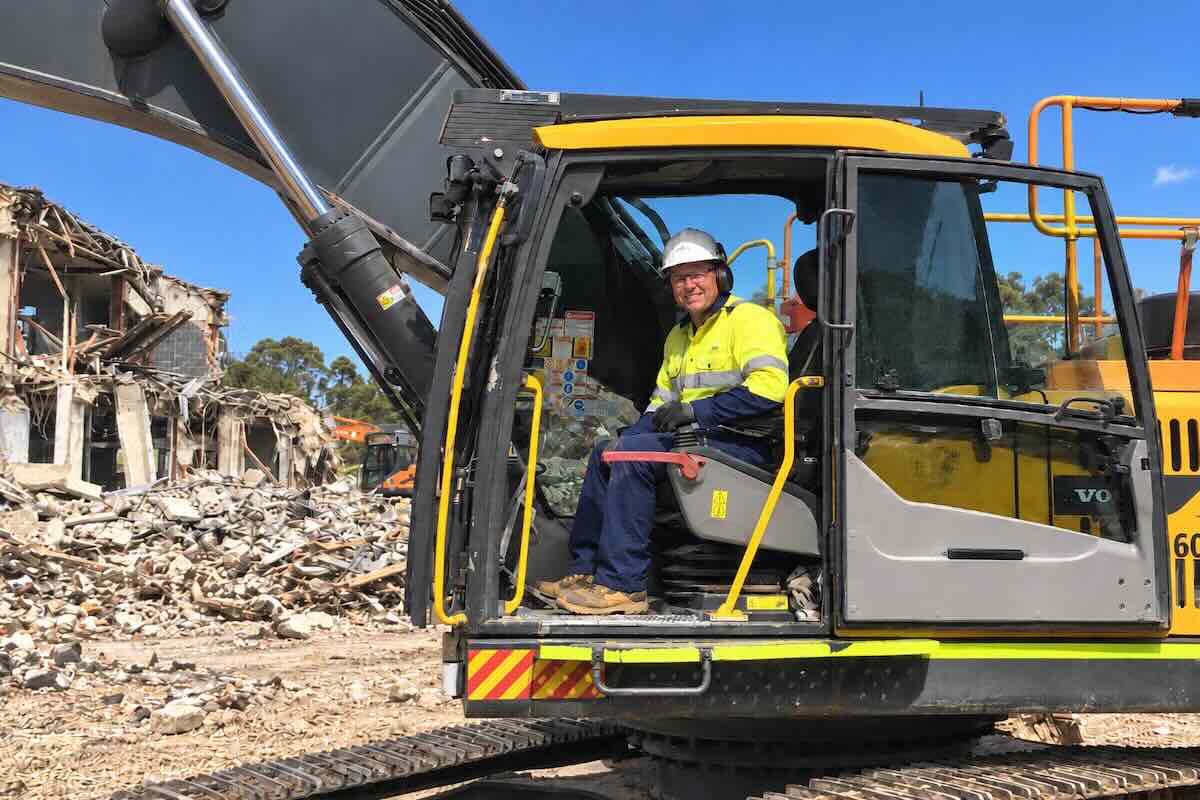 Insured demolition contractor in an excavator in front of a demolition site